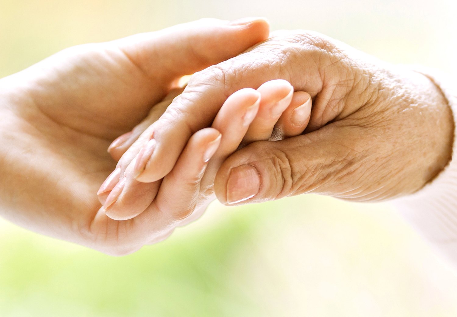 Eine jüngere Hand hält sanft die faltige Hand eines älteren Menschen, symbolisiert Fürsorge, Unterstützung und Vertrauen in der Pflege.