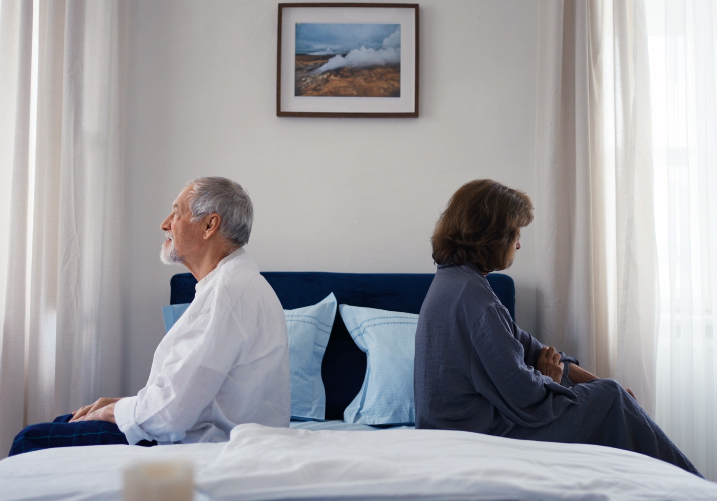 Ein älteres Paar sitzt im Bett mit dem Rücken zueinander